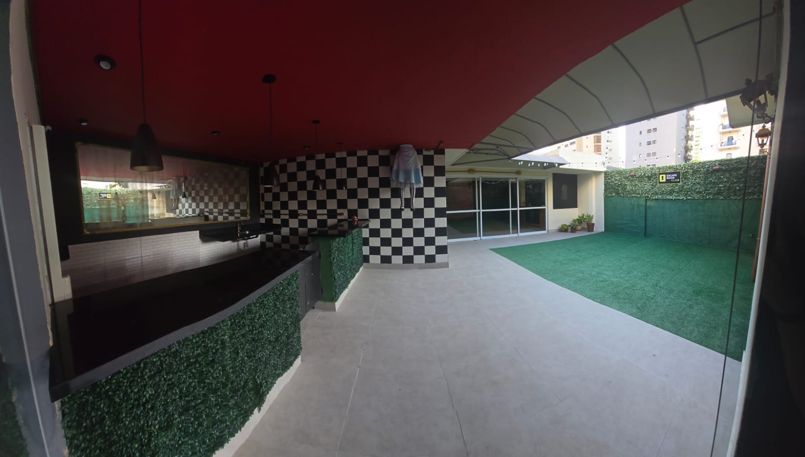 Terraço coberto do Escape Club com bar, parede xadrez e jardim